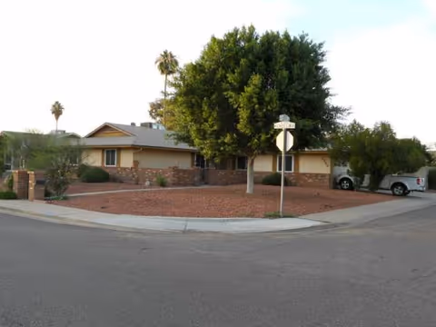 Single-story senior living home with a circular driveway and a large tree in front.