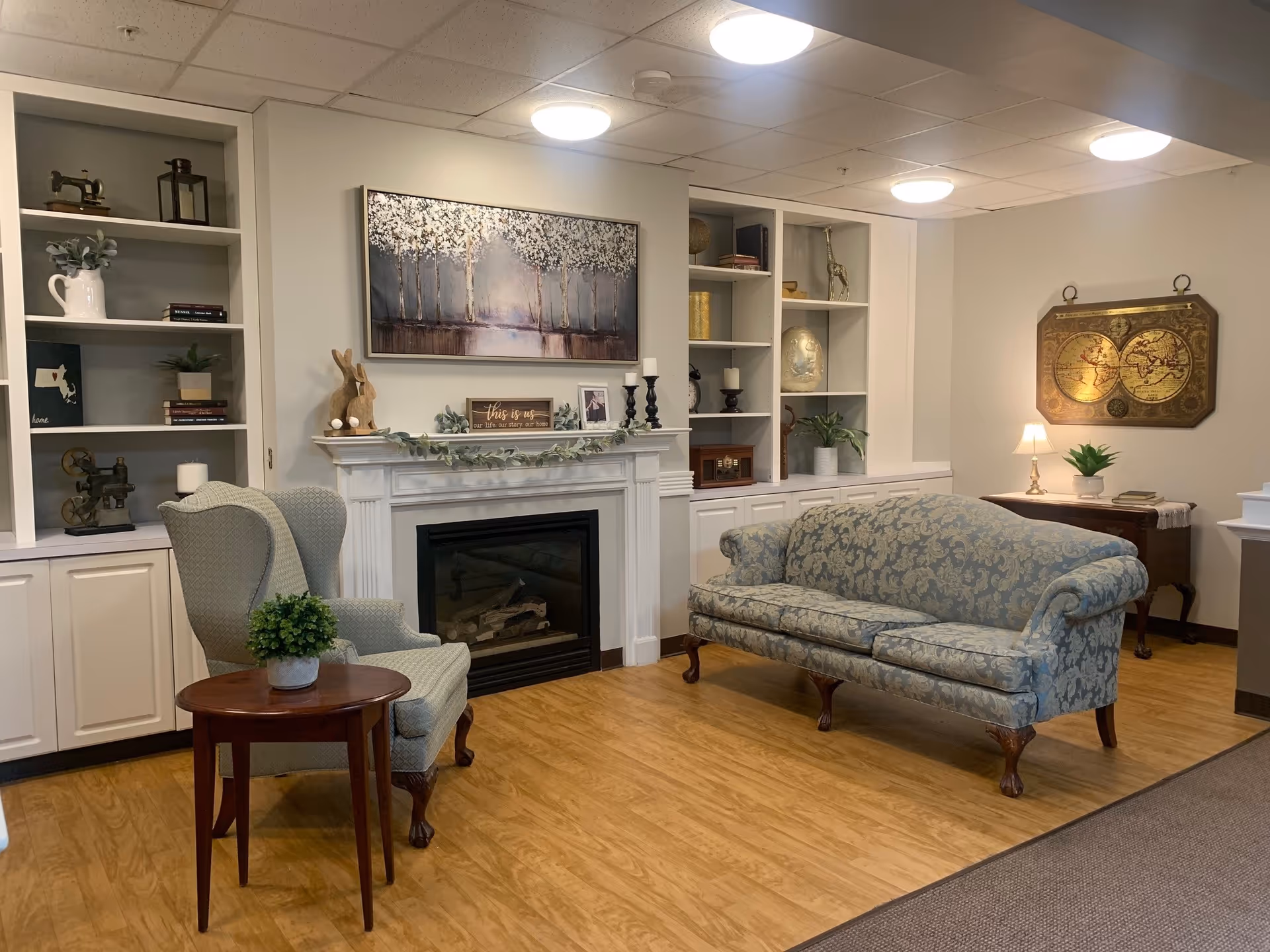 Cozy furnished common living room with a fireplace, patterned sofa, wingback chair, built-in shelves and decorative accents.