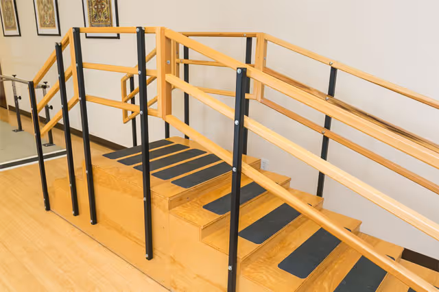Wooden rehabilitation staircase with dual handrails and non-slip treads in an interior therapy area.