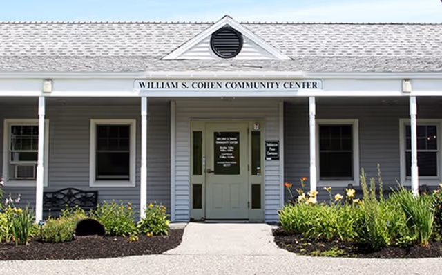 Front entrance of the William S. Cohen Community Center with a covered porch, central door, windows, and landscaped beds.