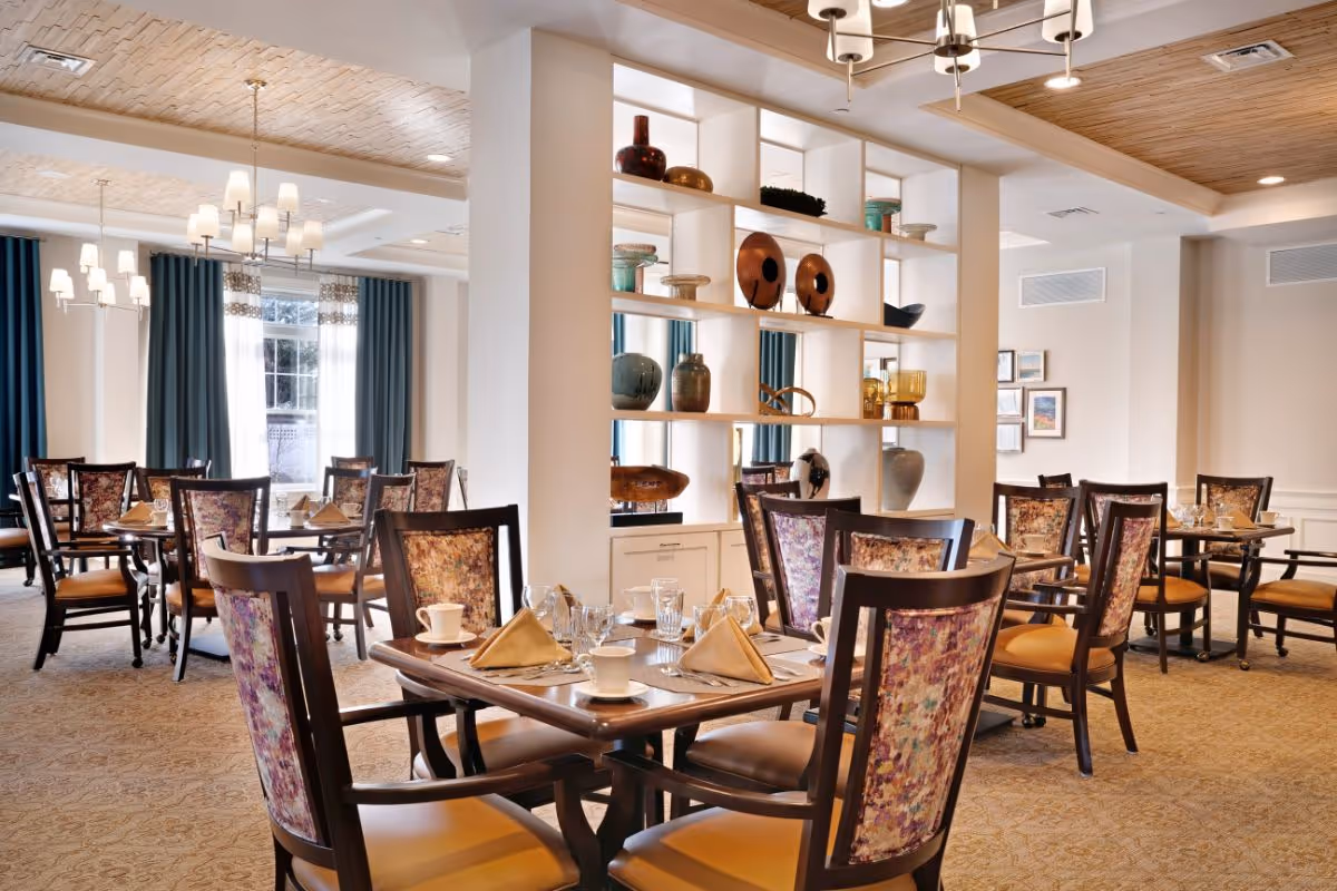 Bright, elegantly furnished dining room with multiple set tables, upholstered chairs, and a decorative shelving divider.