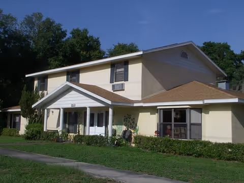 Two-story cream-colored senior care facility with a covered entrance and manicured shrubs.