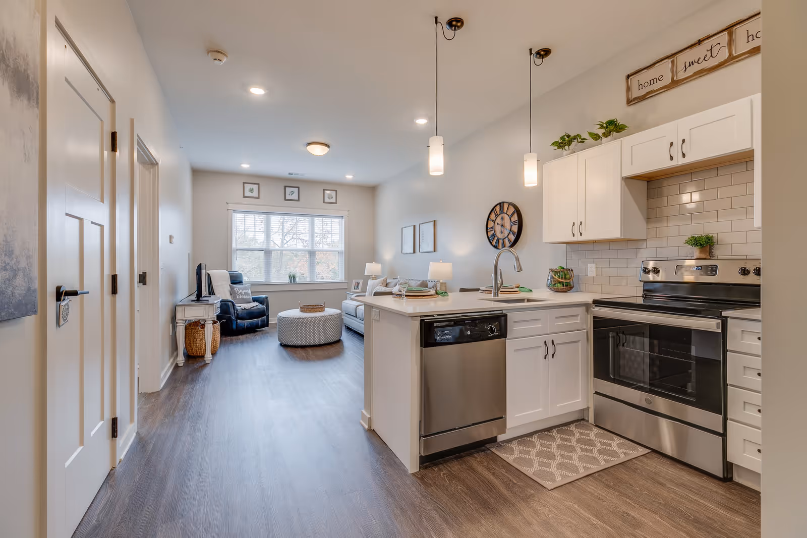 Open-plan kitchen with white cabinets, stainless steel appliances and an island opening into a bright living area.
