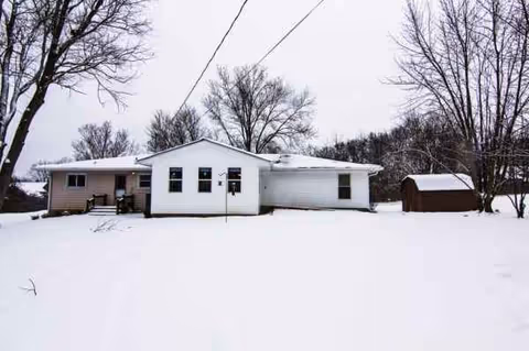 Front view of Our Family Home, a white, single-story facility with a snow-covered yard and shed.