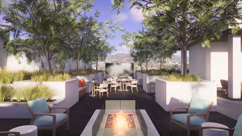 Rooftop outdoor patio with a central fire pit, lounge chairs, dining tables, planter boxes and trees under a blue sky.