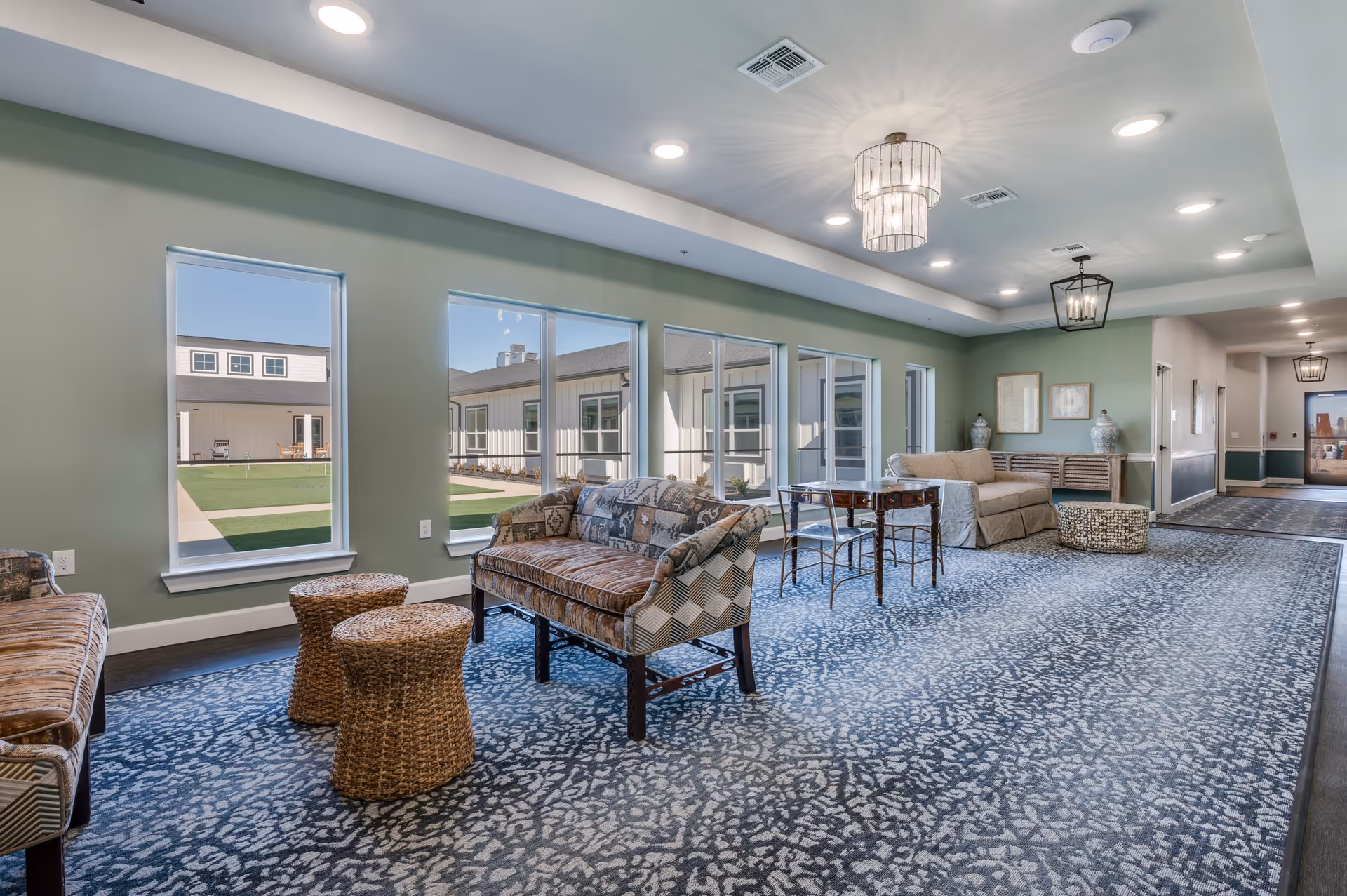 Bright communal lounge with sofas, chairs, wicker stools and large windows overlooking a courtyard.