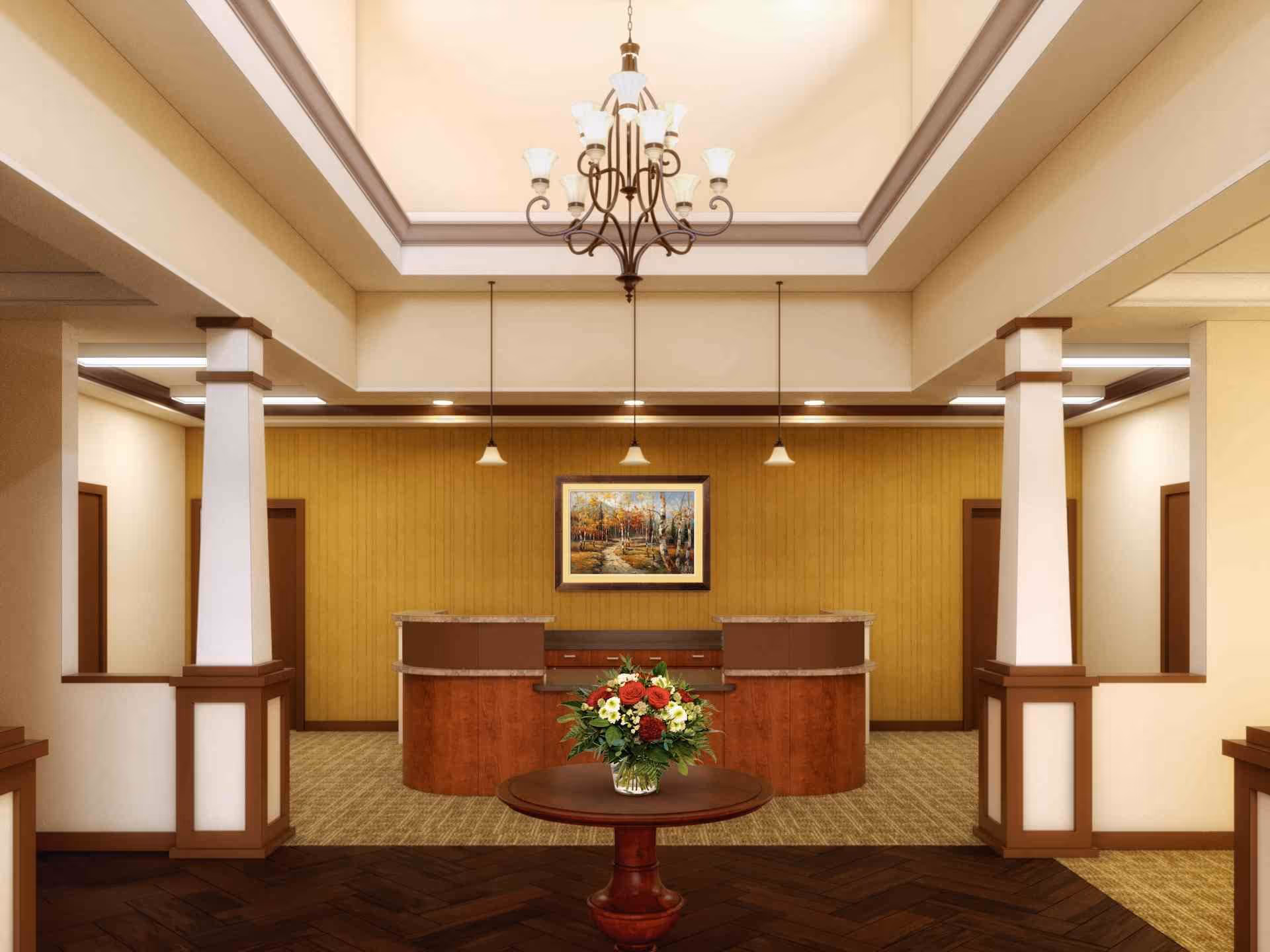 Reception lobby with a central round table holding a flower arrangement, columns, a front desk and a chandelier.