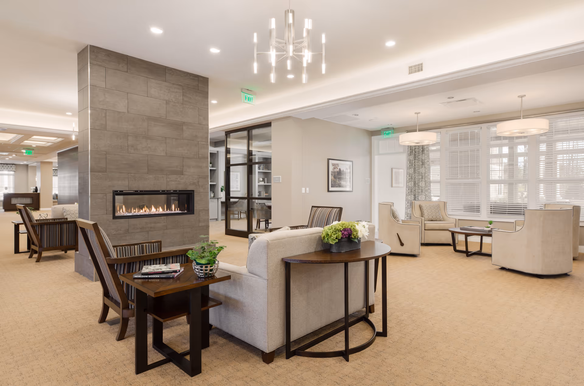 Spacious, well-lit communal living room with sofas and armchairs arranged around a linear fireplace and large windows.