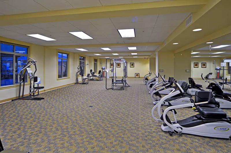 Large interior fitness room with recumbent exercise bikes along the right wall, weight machines in the center, and mirrored walls.