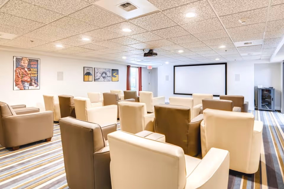 A media room with rows of beige and brown armchairs facing a large projection screen.