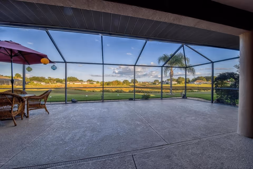 Screened-in patio with wicker seating and a red umbrella overlooking a grassy yard and pond.