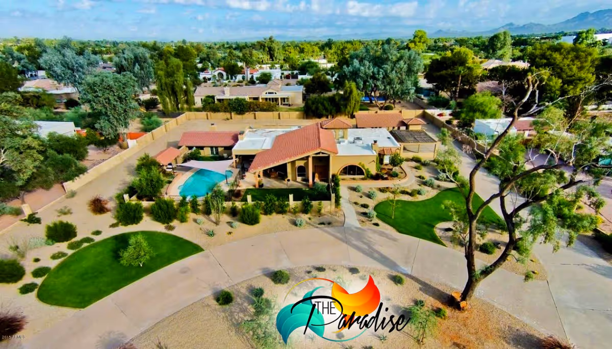 Aerial view of a single-story assisted living facility with a pool, paved driveway, and landscaped desert gardens.