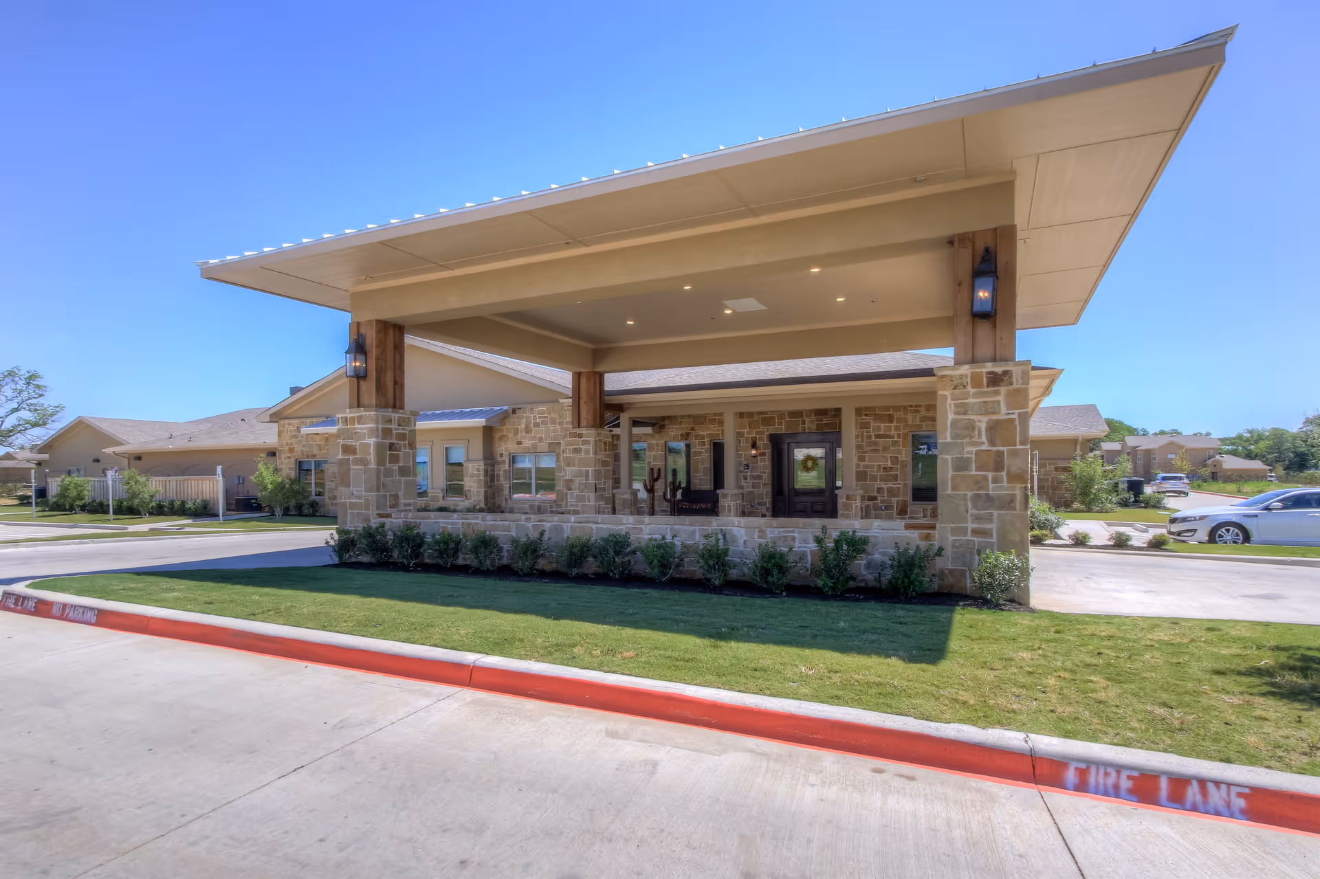 Exterior view of Clear Fork Assisted Living and Memory Care facility showing a covered entrance with stone pillars, a driveway, and a well-maintained lawn under a clear blue sky.