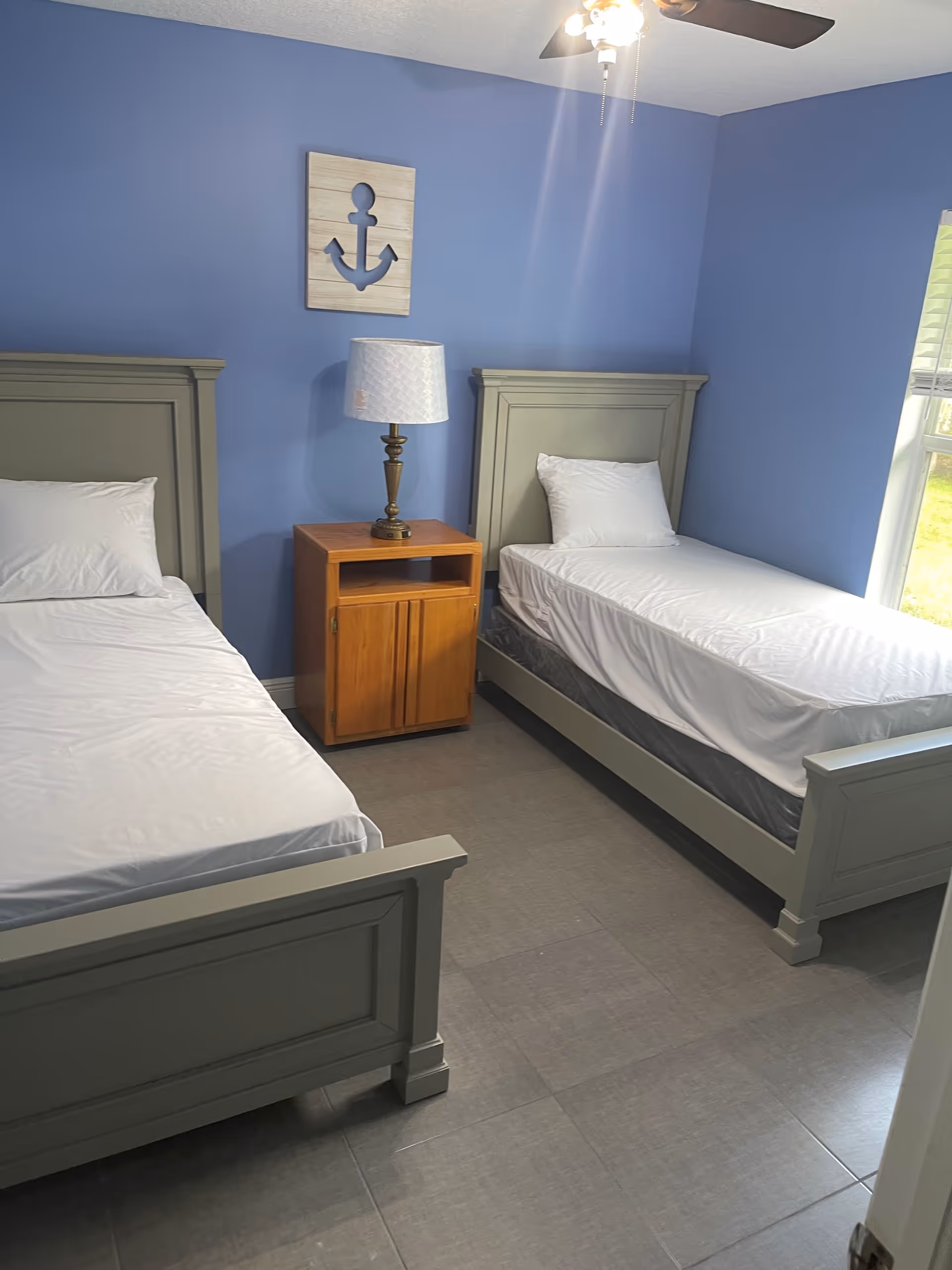 Two twin beds in a blue-walled bedroom with a wooden nightstand and lamp between them.