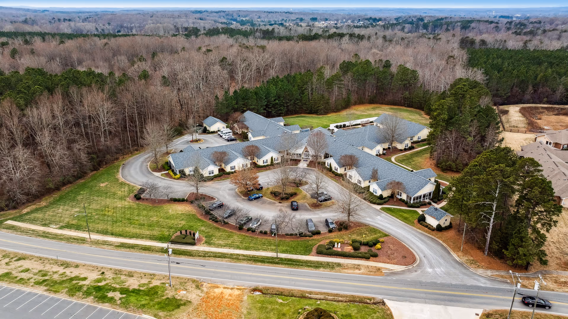 Aerial view of TerraBella Lincolnton senior living facility surrounded by trees and greenery, showing a large building with multiple wings, a circular driveway, and parked cars.