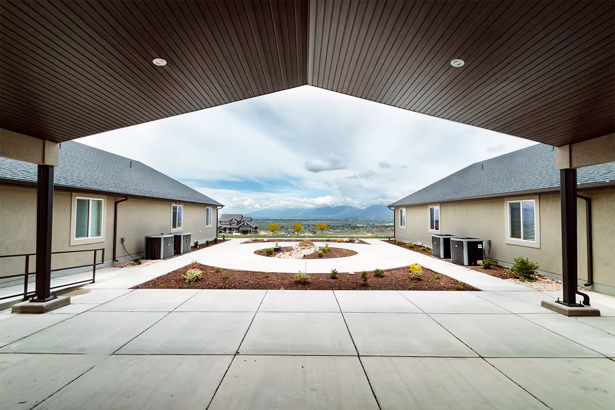 Covered courtyard between single-story assisted living buildings with landscaping and distant mountain views.