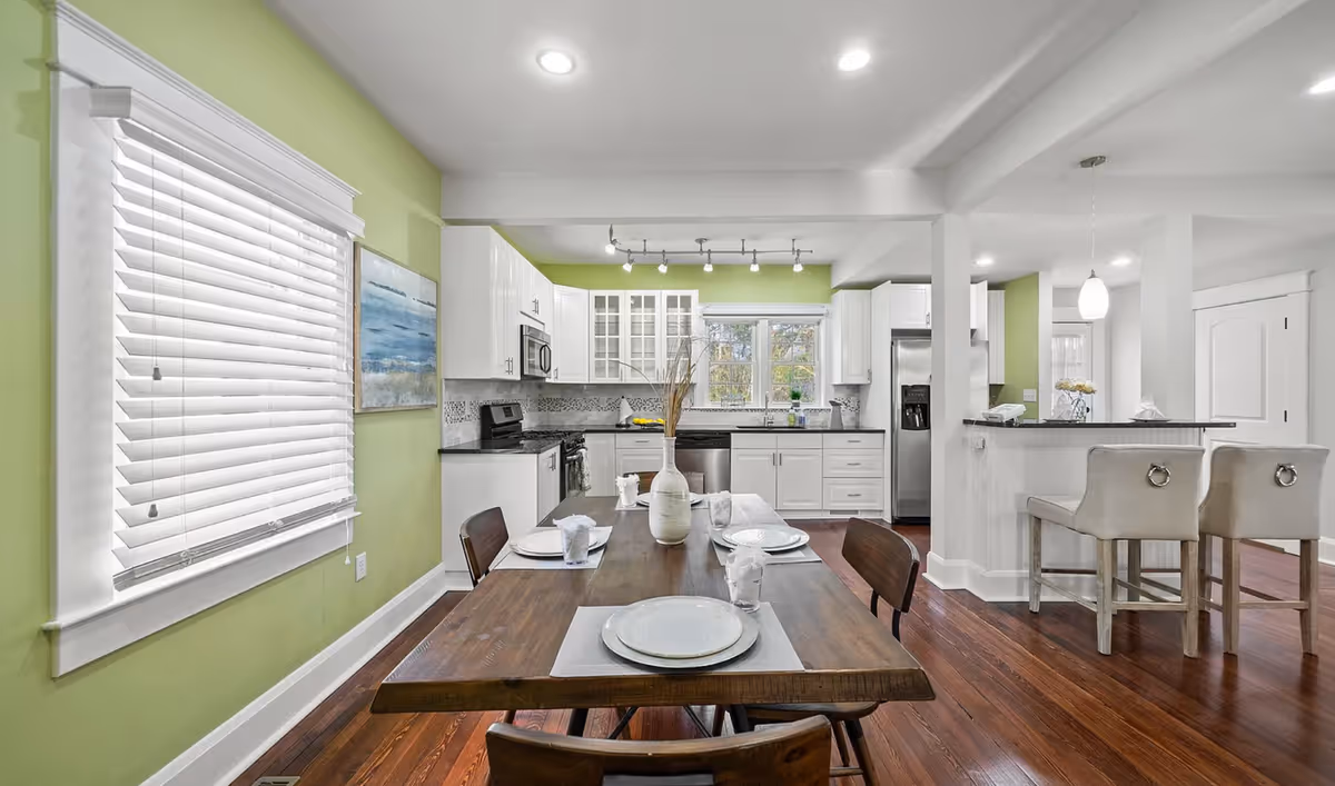 Open-concept dining area with a table set for meals and a bright white kitchen backdrop.