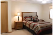 Simple bedroom with a double bed dressed in patterned bedding, a nightstand with a lamp, a closet door, and a window.