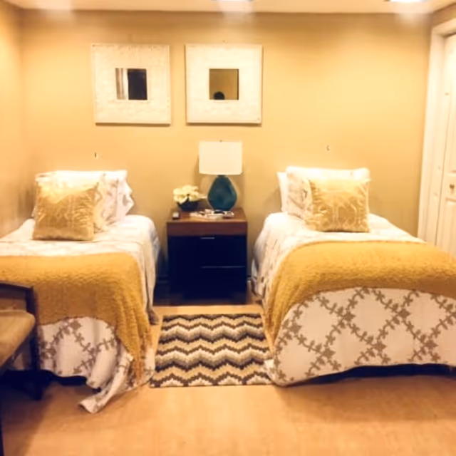 Two twin beds in a warmly decorated bedroom with a nightstand and lamp between them.