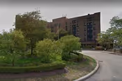 Exterior view of a multi-story brick senior living building with a curved driveway and greenery.