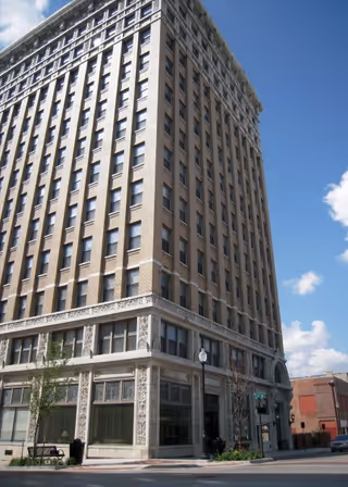 Tall brick building on a street corner, with many windows and decorative lower façade.
