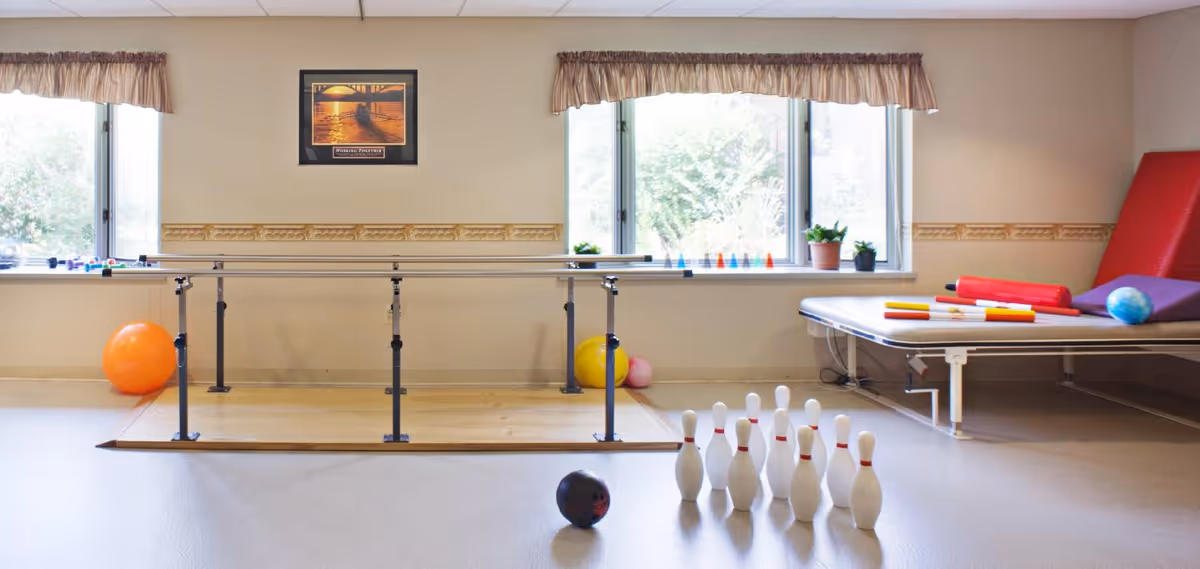 Rehabilitation/exercise room with parallel bars, a therapy table, exercise balls and a set of bowling pins.