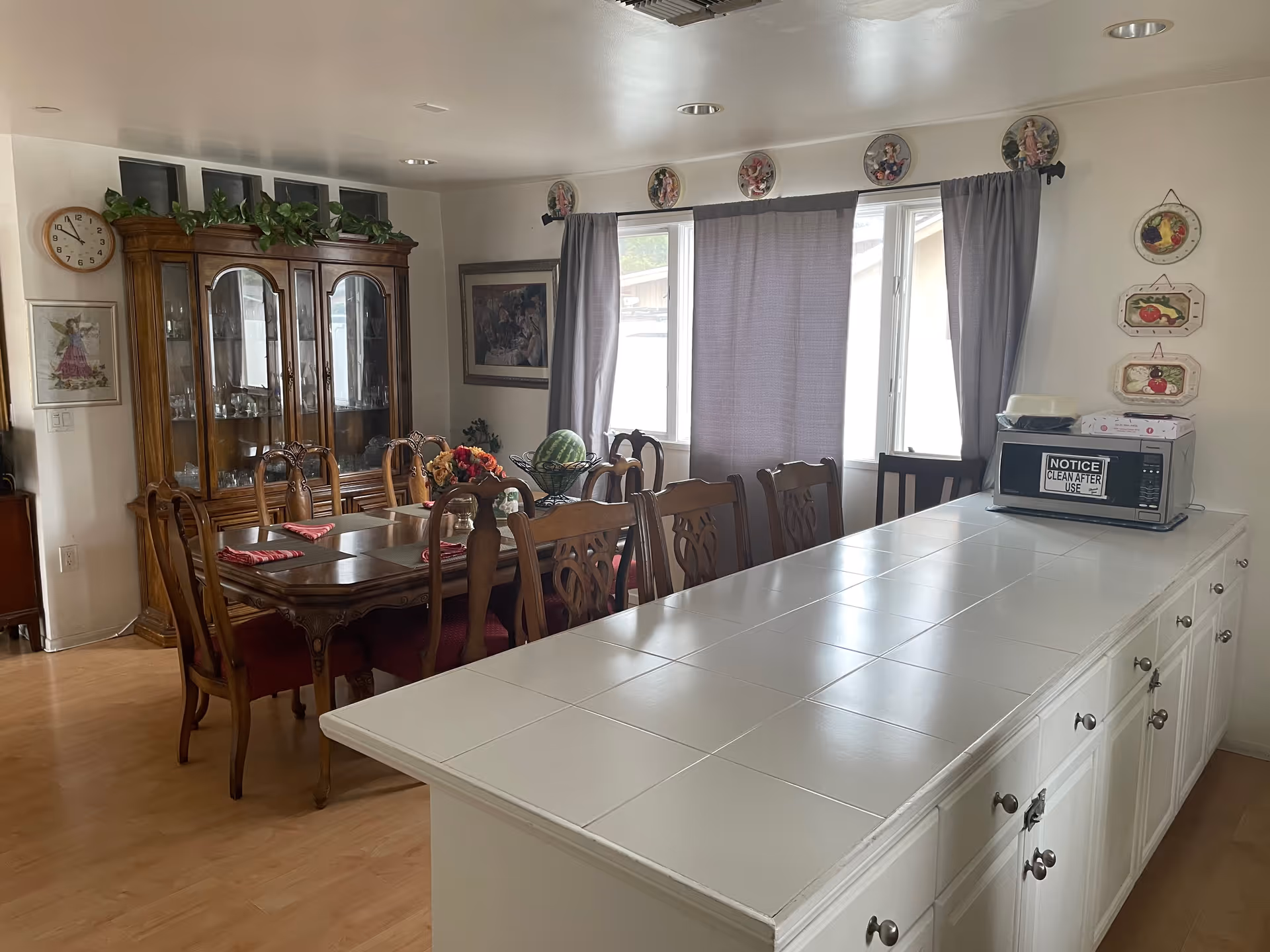 Open dining area with a wooden dining table and chairs beside a white tiled kitchen island and a china cabinet.