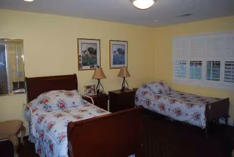 Two twin beds with floral bedspreads in a yellow-walled senior living bedroom.