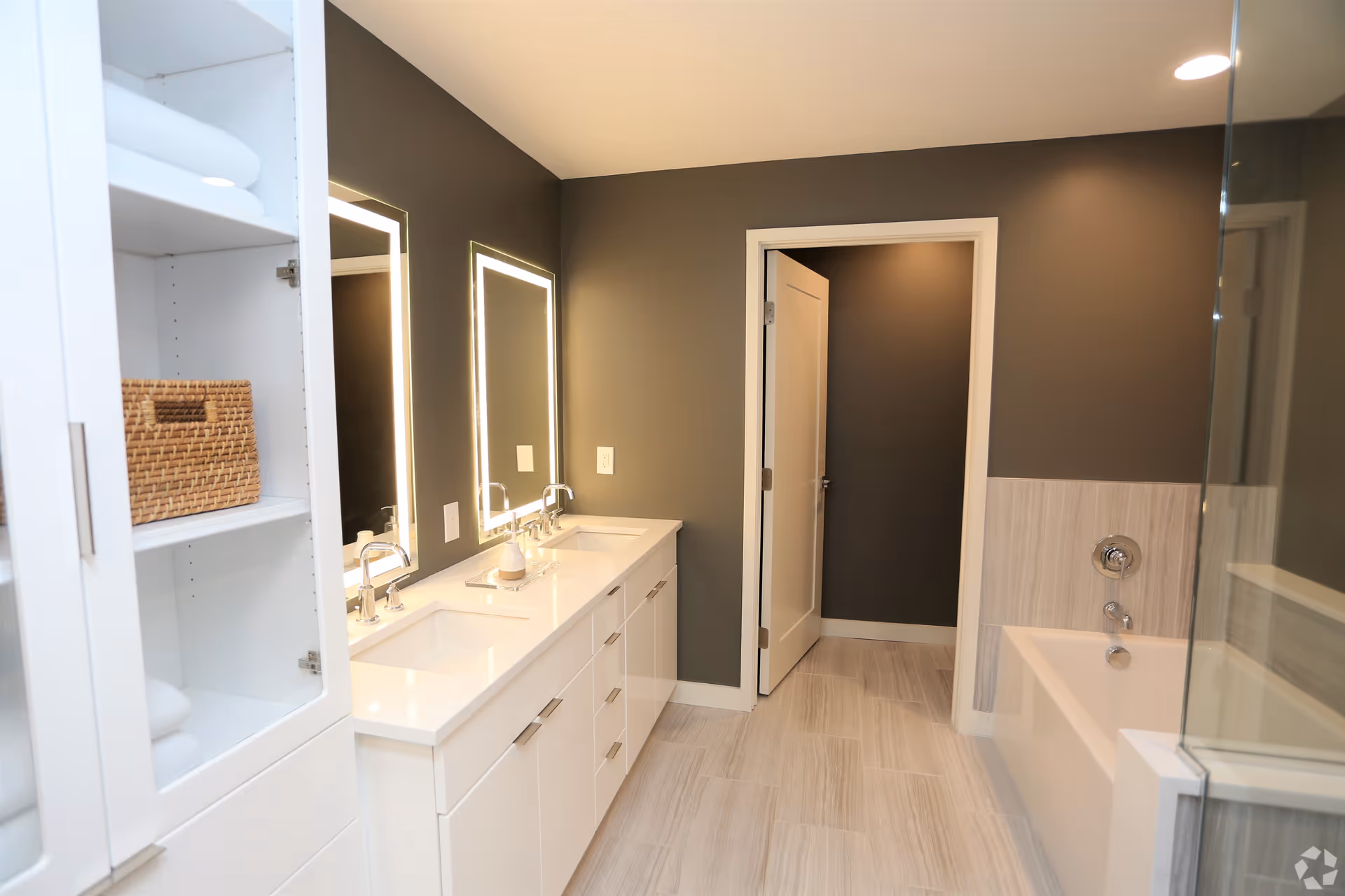 Modern bathroom with double sink vanity and illuminated mirrors, built-in shelving, bathtub and glass shower.