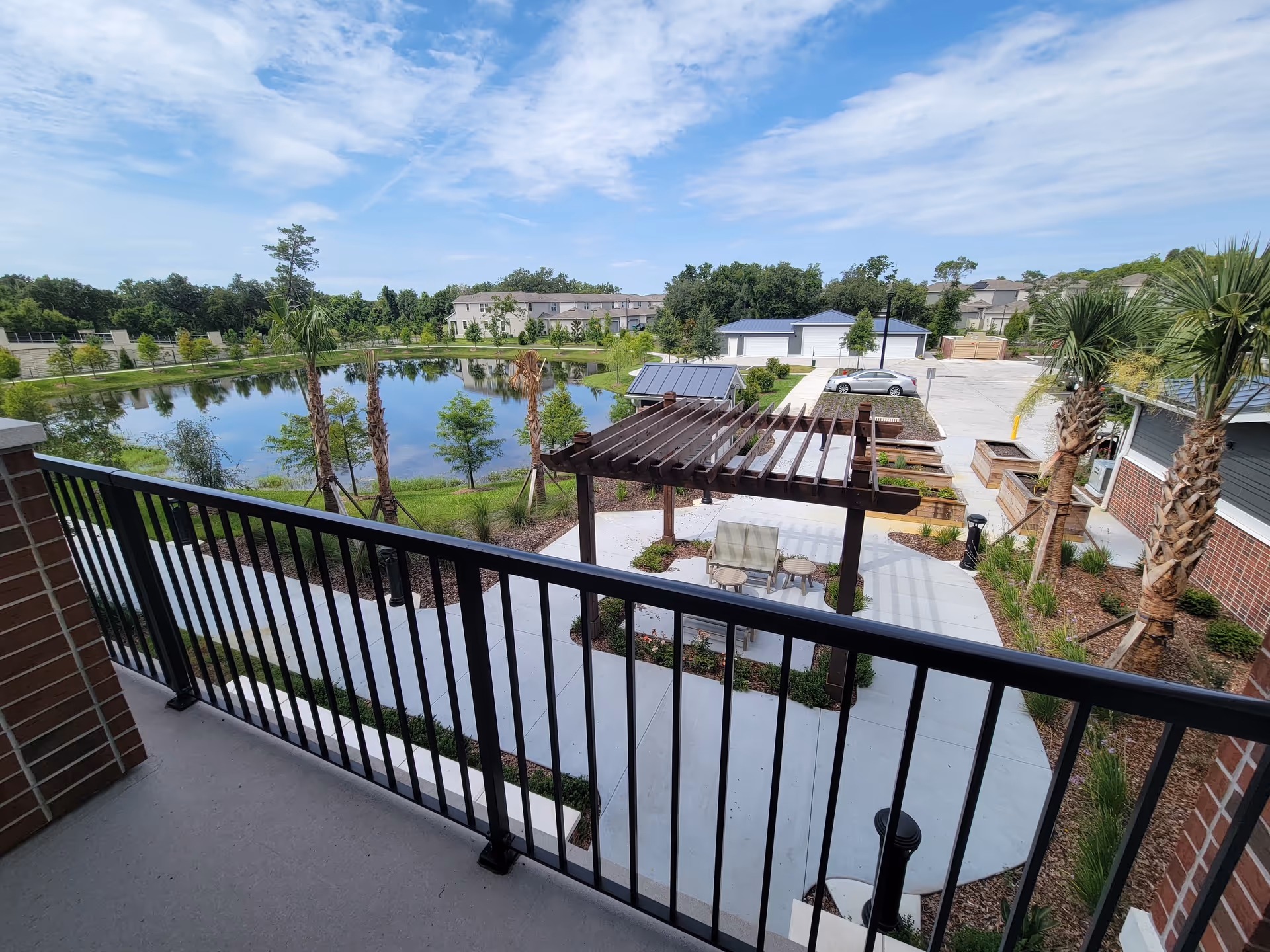 View from a balcony over a landscaped courtyard with a pergola, seating, palm trees, and a pond in the background.