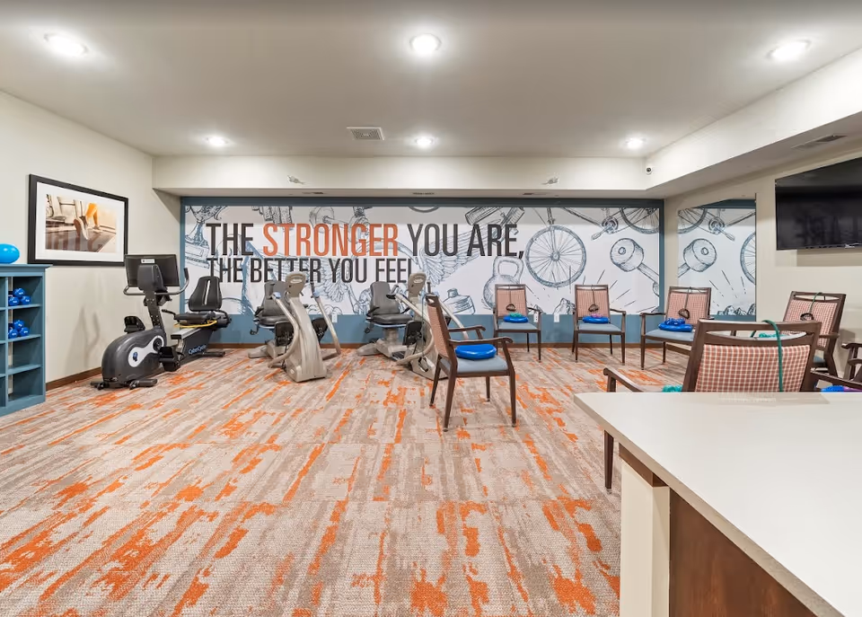 Interior fitness/activity room with recumbent exercise bikes, chairs and a large wall mural reading "The stronger you are, the better you feel."