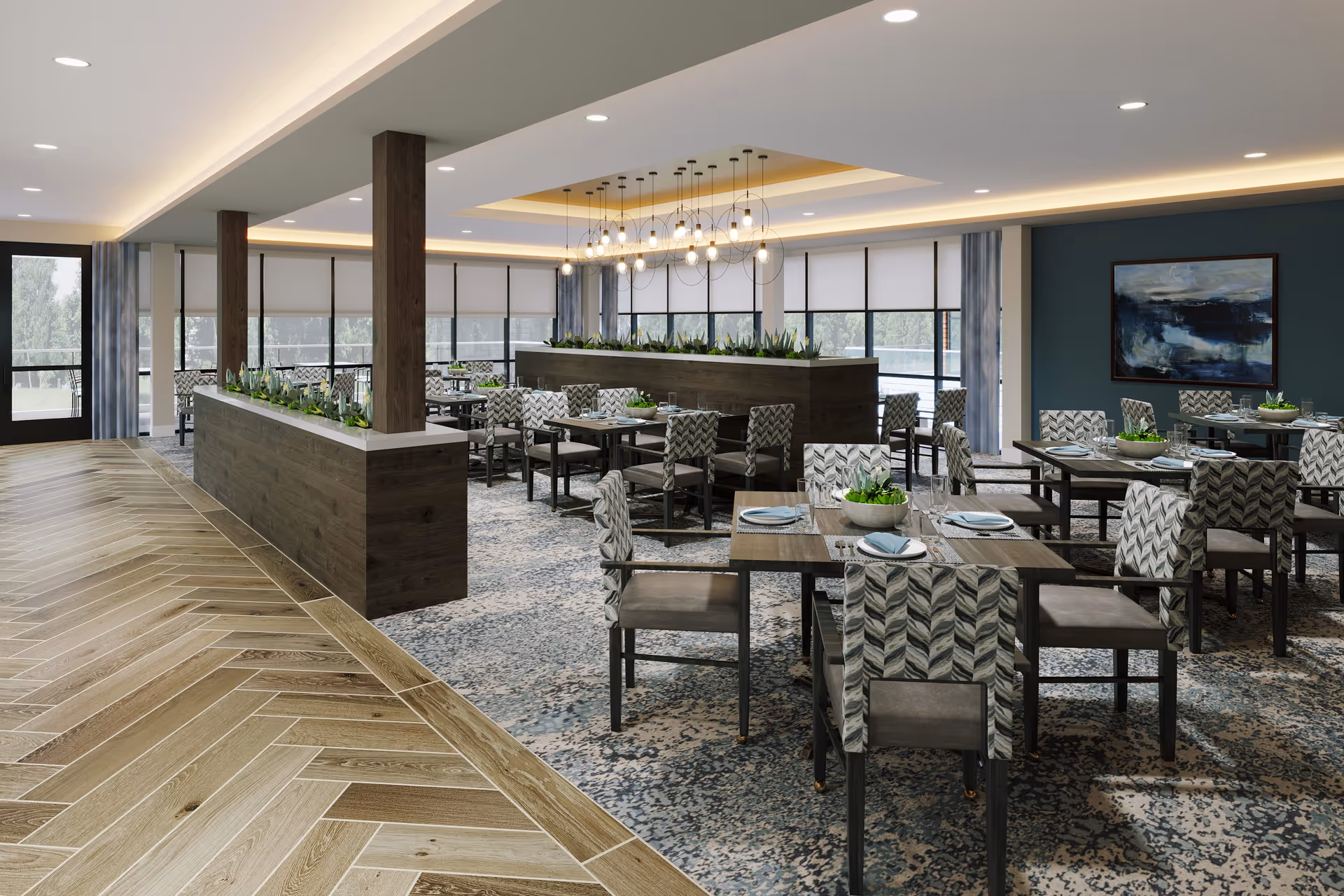 A spacious dining room with multiple tables and chairs arranged neatly. The chairs have patterned upholstery, and the tables are set with plates, napkins, and small green plants as centerpieces. Large windows with roller shades allow natural light to fill the room. The ceiling features modern pendant lighting and recessed lights, and there are wooden pillars and planters dividing the space. The floor has a combination of wood and patterned carpet.