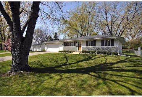 Single-story white senior care building with a manicured lawn and large trees.