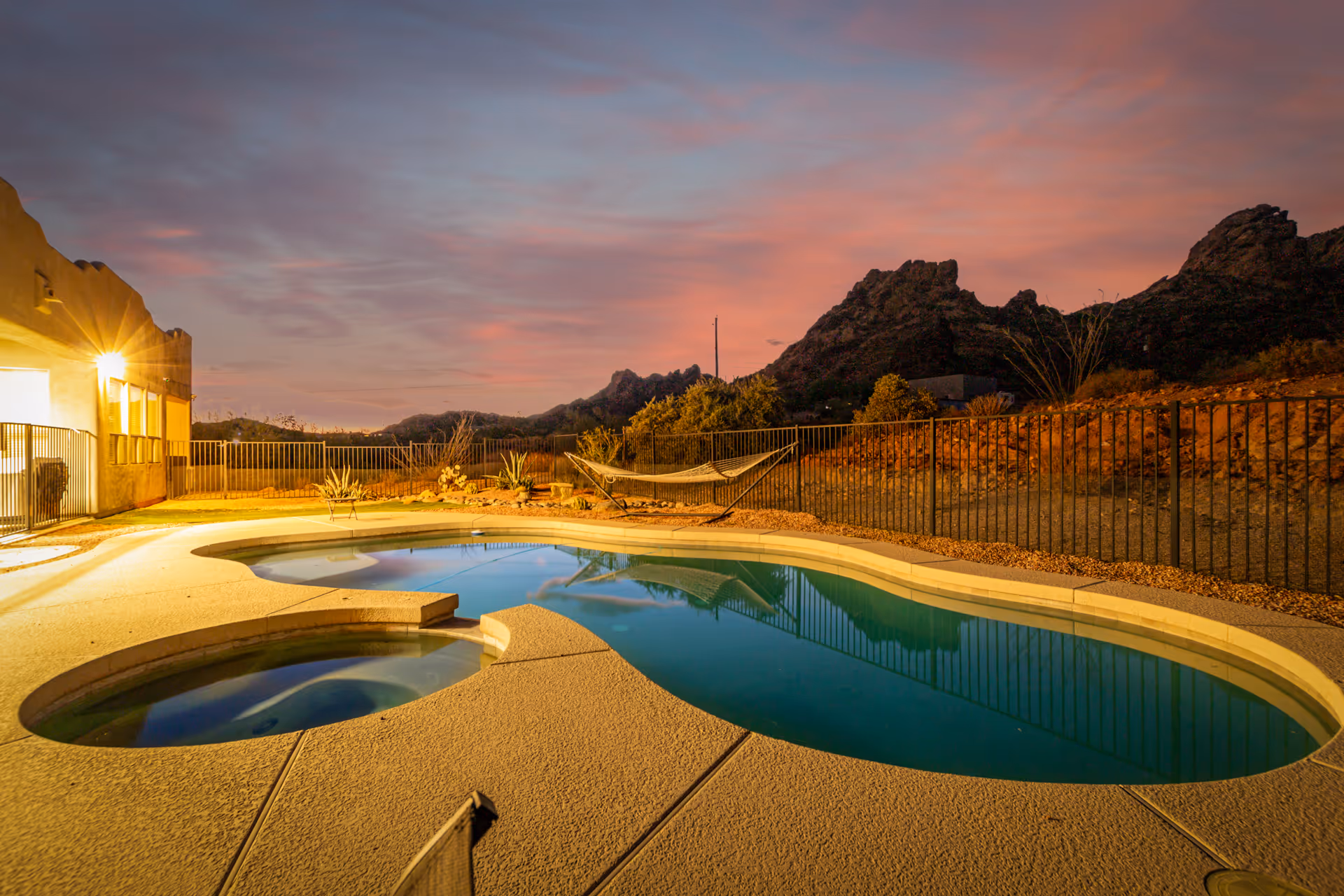 Outdoor pool area at sunset with mountains and hammock, building lit on left.