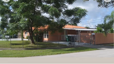 Front view of a single-story brick senior home behind a chain-link fence.