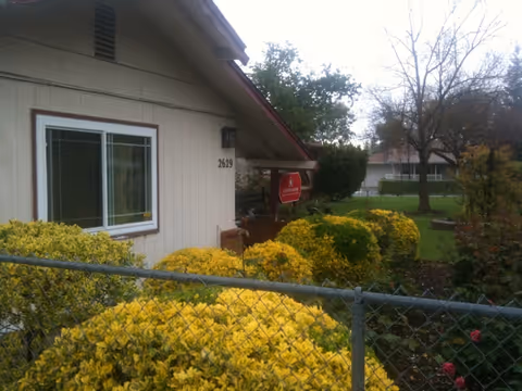 Exterior view of a senior living facility with yellow bushes, fence, and a red stop sign.