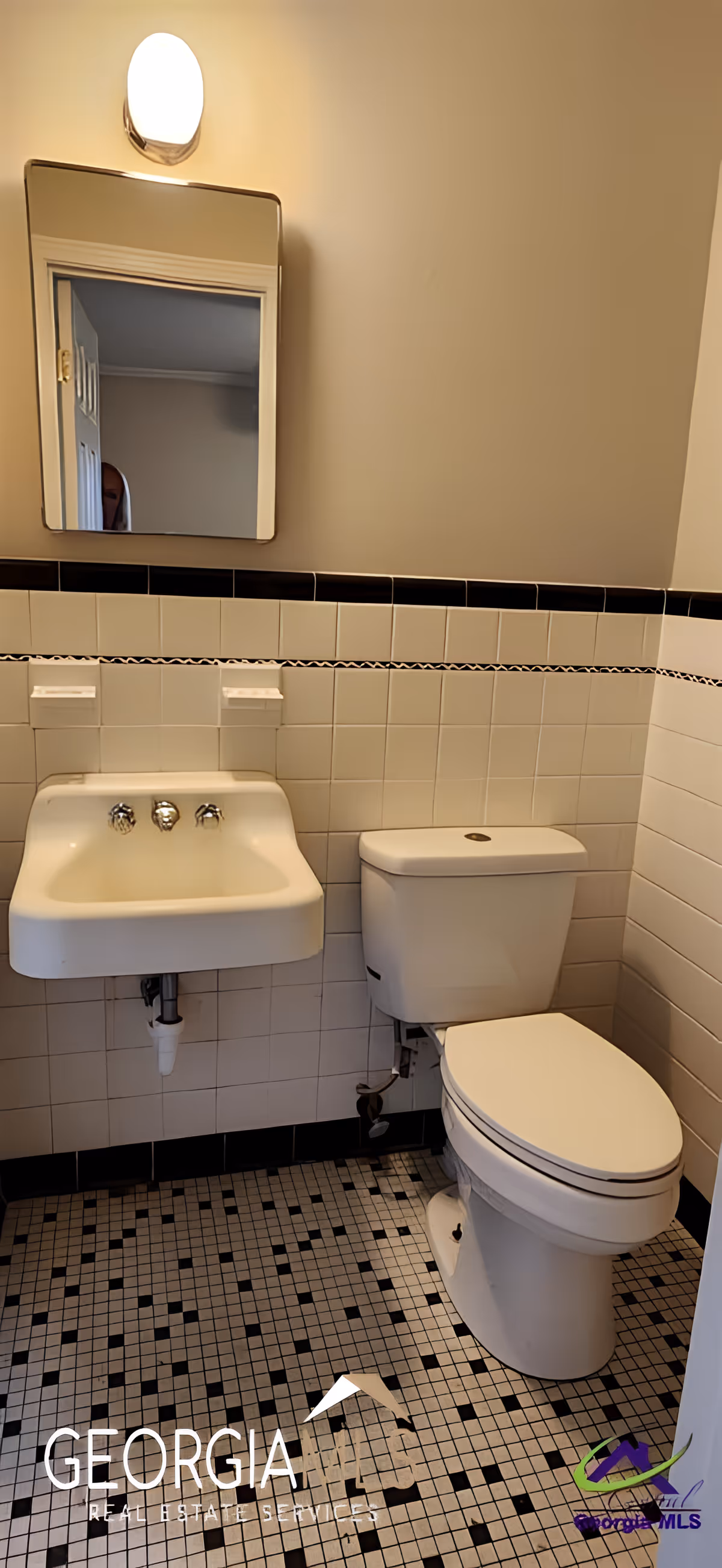 Small tiled bathroom with a wall-mounted sink, toilet, mirror, and overhead light.
