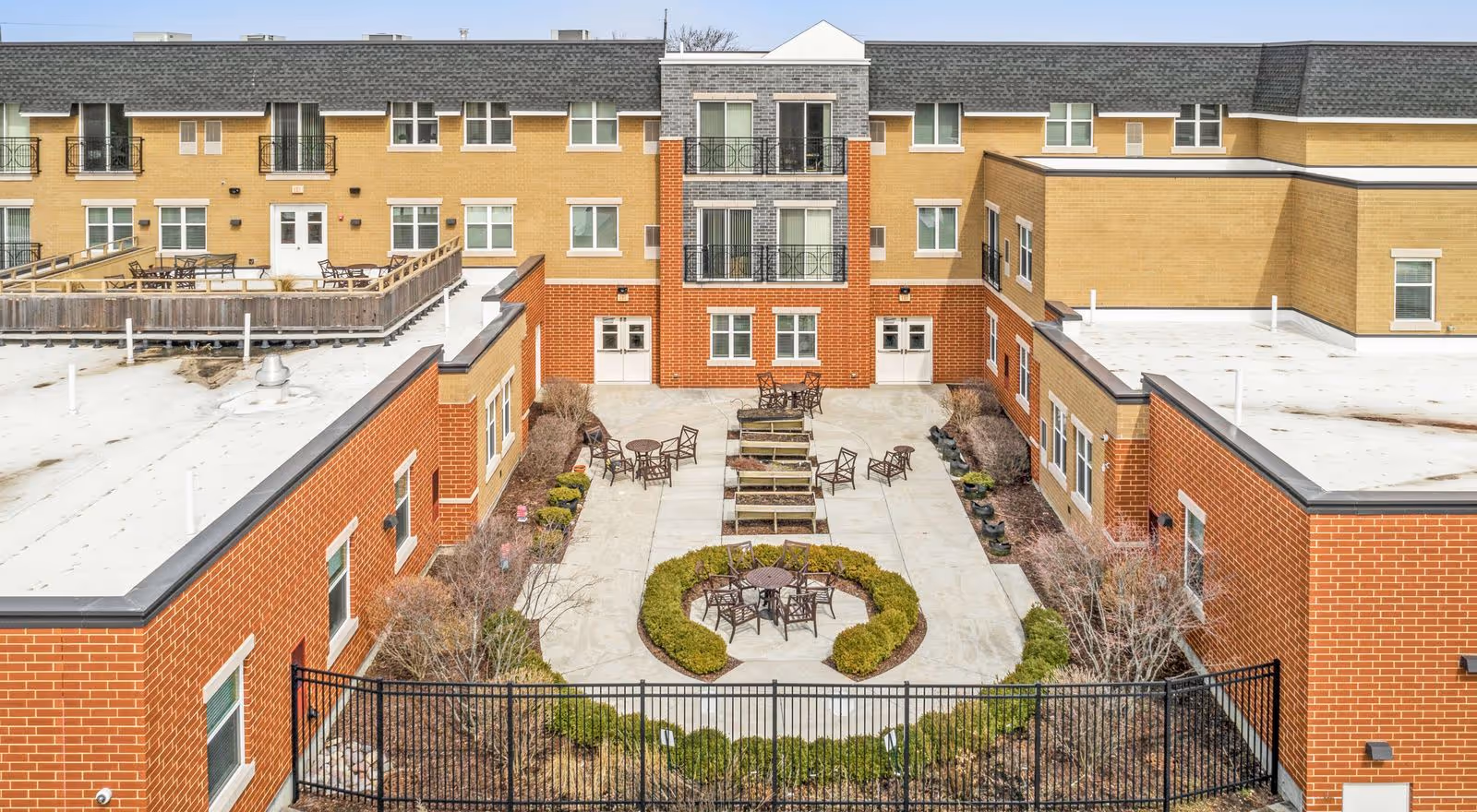 A central outdoor courtyard with patio tables, chairs and landscaped planters surrounded by a three-story senior living building.