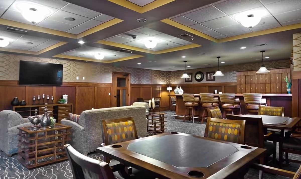 Communal lounge with sofas, game tables and a bar counter in a senior living facility.