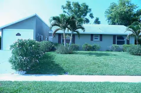 Front exterior of a single-story senior living facility with a green lawn and palm trees.