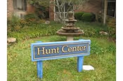Blue sign reading 'Hunt Center' in a grassy courtyard with a fountain and a brick building in the background.