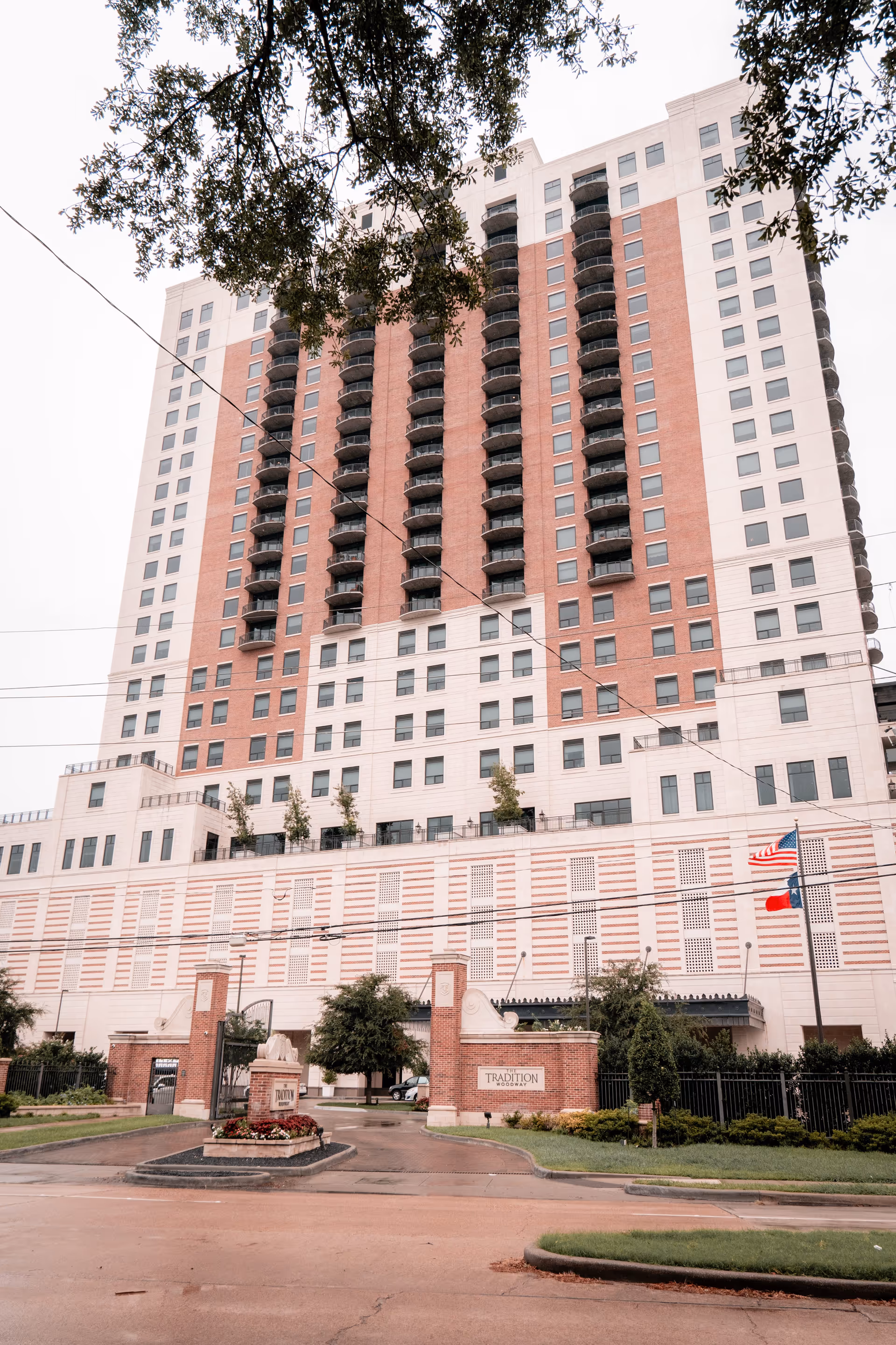 Tall multi-story brick and white residential building with rows of balconies and a gated entrance sign reading 'Tradition'.
