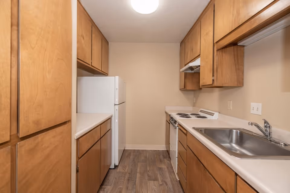 Small galley kitchen with wood cabinets, a white refrigerator and stove, and a stainless steel sink.