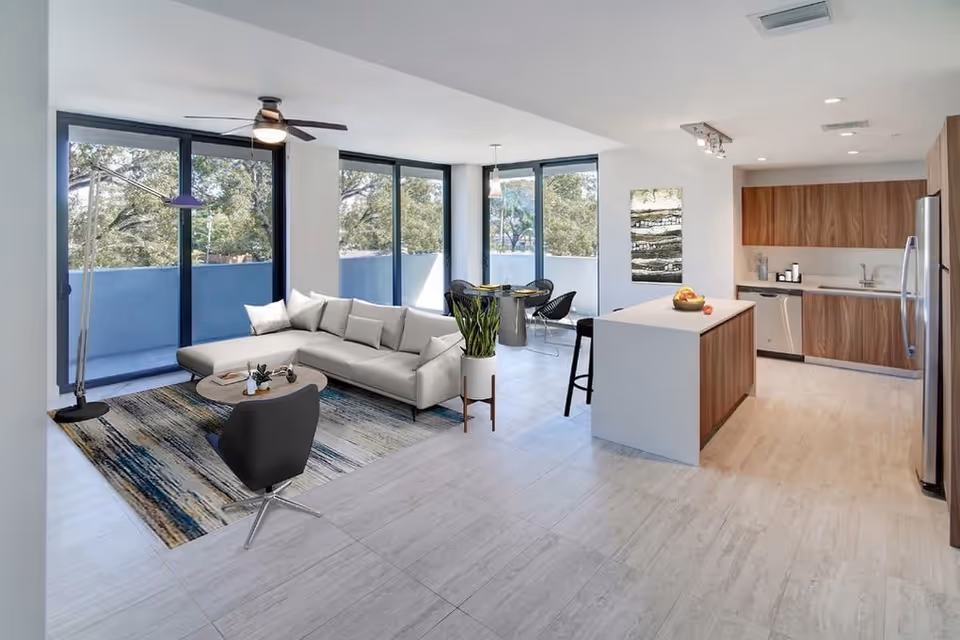 Bright open-concept living room and kitchen with large windows, a sectional sofa, area rug, and a central island.