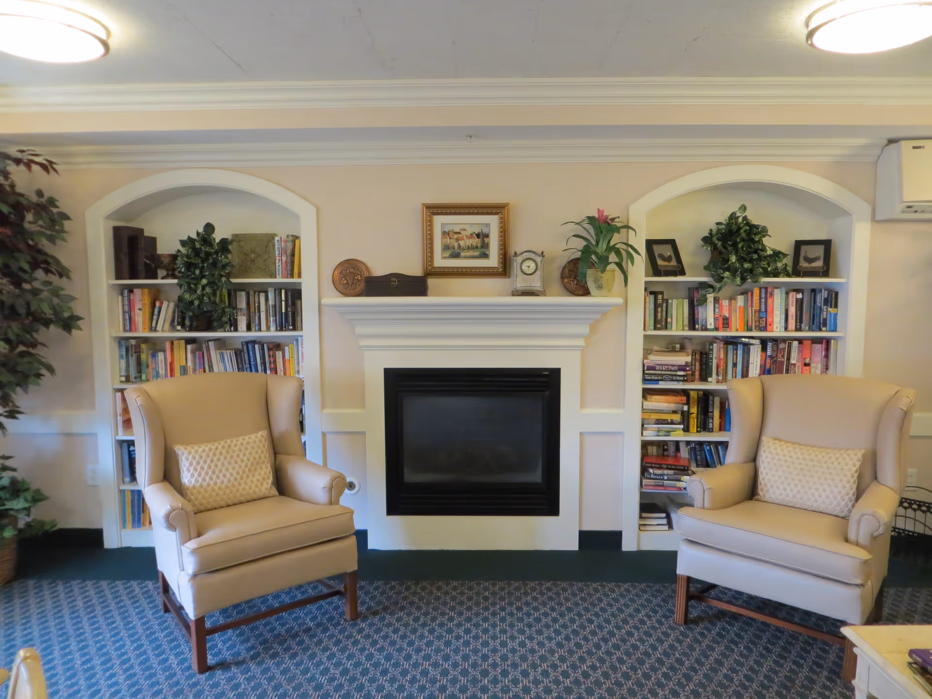 Cozy sitting area with a central fireplace flanked by built-in bookshelves and two beige wingback chairs.