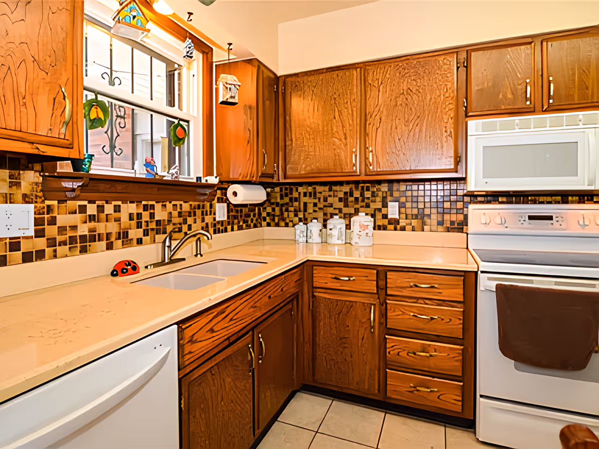 Well-lit kitchen with wooden cabinets, tiled backsplash, a sink under a window, countertop appliances, dishwasher and stove.