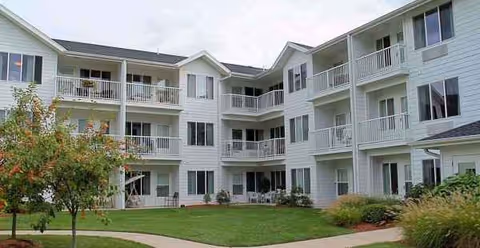 A light-colored, multi-story senior living building with balconies surrounding a landscaped courtyard.