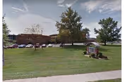 Front lawn and parking area of Milton Rehabilitation & Nursing Center with the building in the background and a campus sign on the grass.