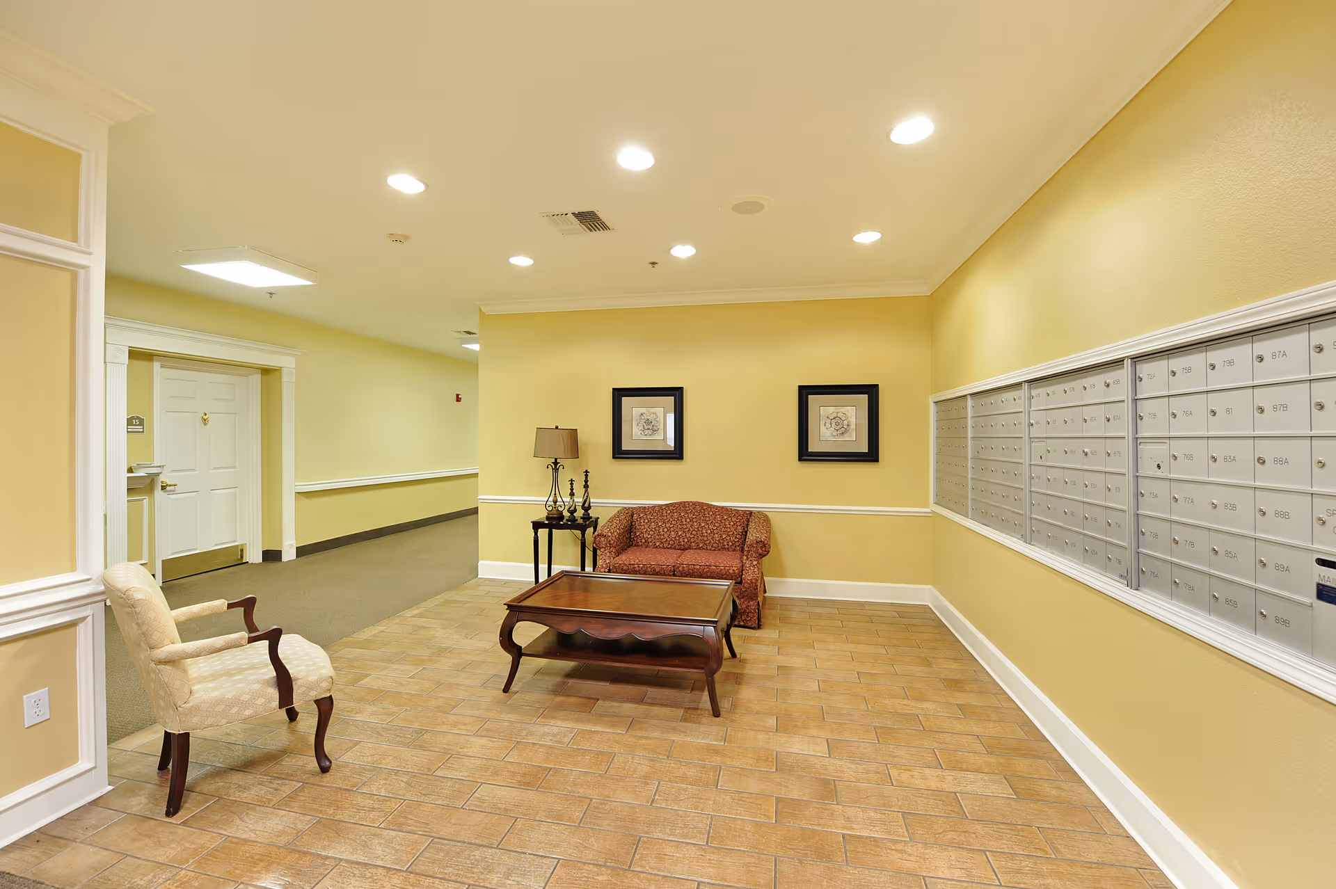 Well-lit lobby seating area with mailboxes along the right wall, a sofa, chairs, and a coffee table.