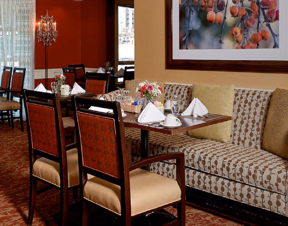 Dining room with set tables, upholstered chairs and banquette seating decorated with napkins, glassware and flowers.